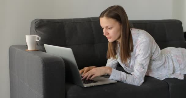 Focused millennial female freelancer working remotely online, reading news, on comfortable couch remotely at home. woman coughs and works at home in quarantine - Кадры, видео