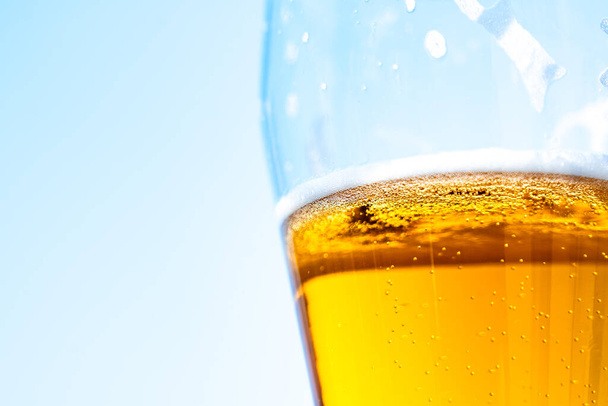 Light beer in a glass goblet on a background of blue sky. Beer foam on the walls of a glass in the sunlight - Foto, Imagen