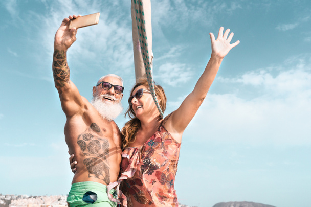Starsza para biorąc selfie z mobilnym smartfonem na wakacje żaglówka - Szczęśliwi dojrzali ludzie dobrze się bawią świętując rocznicę ślubu na wycieczkę łodzią - Love relationship and travel lifestyle concept - Zdjęcie, obraz