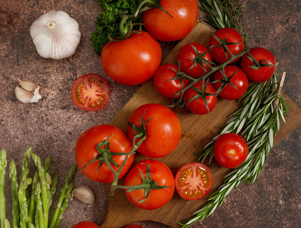 Red tomatoes, thyme, rosemary, garlic, parsley and asparagus on rustic rusty background. Top view, flat lay, view from above. Concept of healthy food ingredients - Foto, Bild
