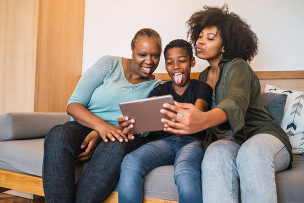 Portrait of African American grandmother, mother and son taking a selfie with digital tablet at home. Technology and lifestyle concept. - 写真・画像