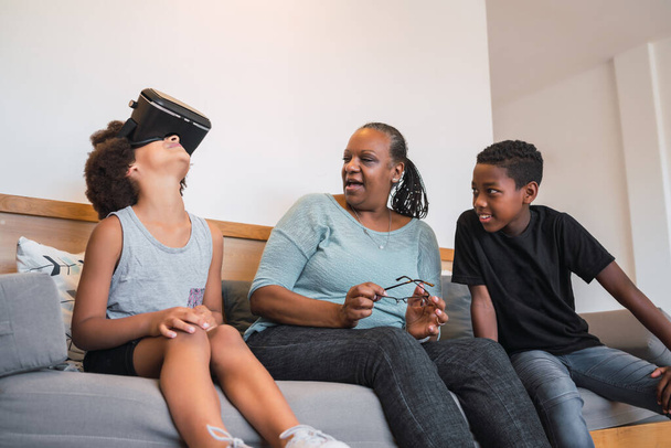 Portrait of African American grandmother and grandchildren playing together with VR glasses at home. Family and technology concept. - Фото, изображение