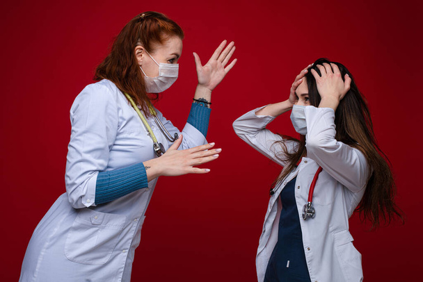 Портрет двух женщин-врачей в медицинской одежде с фонендоскопом вокруг шеи спорят, картина изолирована на красном фоне
 - Фото, изображение
