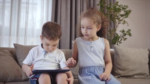 Cute family and daughter,sister-in-law a nanny with little brother,looking at the screen of a tablet on a cell phone, daughter and her brother are sitting on a sofa, playing at home on a smartphone. - Séquence, vidéo