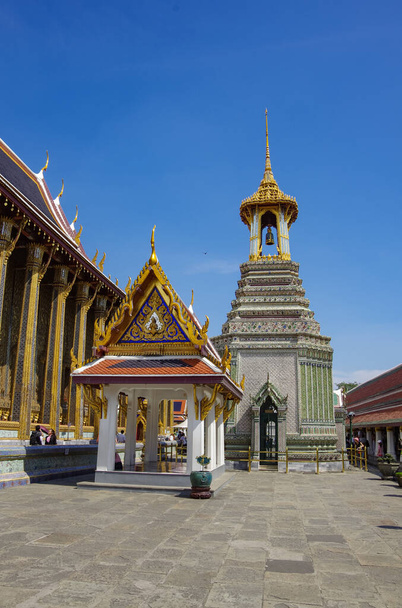 Een Thaise traditionele klokkentoren (belfort) met gedetailleerde, mozaïek kunstwerken en goudkleurig ontwerp bij Wat Phra Kaew (Tempel van de Smaragdgroene Boeddha) in de wijken van het Grand Palace van Bangkok - Foto, afbeelding