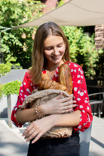 портрет улыбающейся девочки-подростка с упаковкой хлебобулочных изделий в руках
 - Фото, изображение