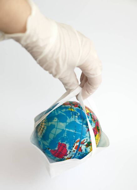 a globe hanging in a protective mask on the hands of a person, as a symbol of the fact that everything is in the hands of a person - Photo, Image
