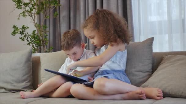 Cute family and daughter,sister-in-law a nanny with little brother,looking at the screen of a tablet on a cell phone, daughter and her brother are sitting on a sofa, playing at home on a smartphone. - Metraje, vídeo