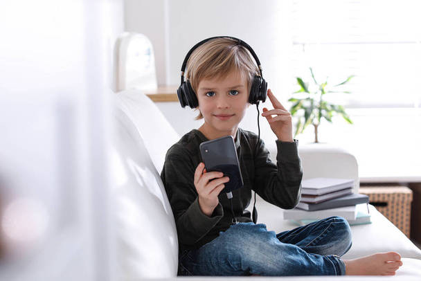 Cute little boy with headphones and smartphone listening to audiobook at home - Foto, Imagem