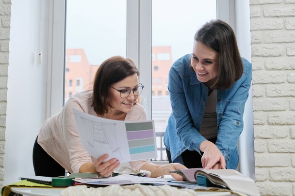 Two women designers working with fabric samples for interior. Choosing fabrics for curtains, furniture upholstery, calculating cost - Foto, afbeelding