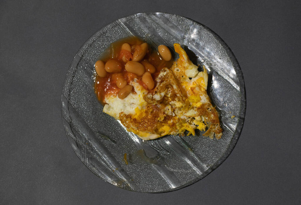 paistettuja munia ja papuja tomaatissa lautasella, jossa on haarukka eristetyllä pohjalla
 - Valokuva, kuva