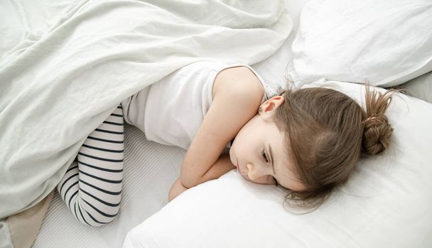 Küçük tatlı bir kız beyaz bir yatakta uyuyor. Çocuk gelişimi ve uyku kavramı. Yukarıdan görünüşü. - Fotoğraf, Görsel