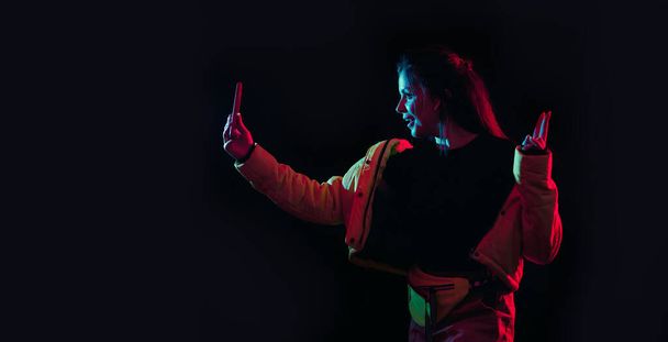 Tik tok рекламная концепция: молодая девушка позирует со смартфоном в руках, делая селфи на черном фоне. TIK TOK - популярная социальная сеть в Интернете.
 - Фото, изображение