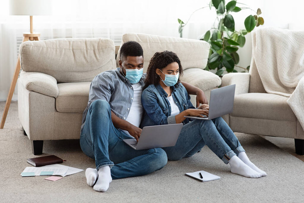 Önálló, elszigetelt házaspár, akik otthon laptopon dolgoznak, orvosi maszkot viselnek. - Fotó, kép