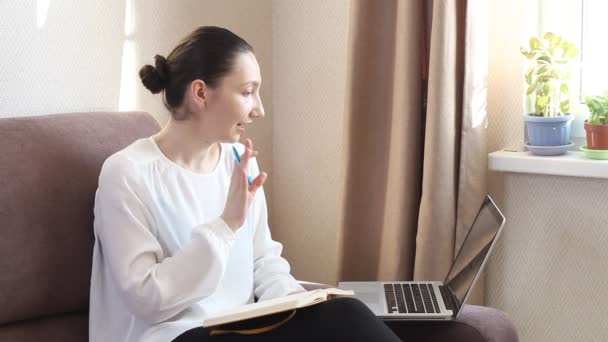 Mladá žena poslouchá online lekce nebo webinář a píše poznámky. Koronavirová pandemie. Zůstat doma na sociální distanční izolaci vlastní karantény - Záběry, video