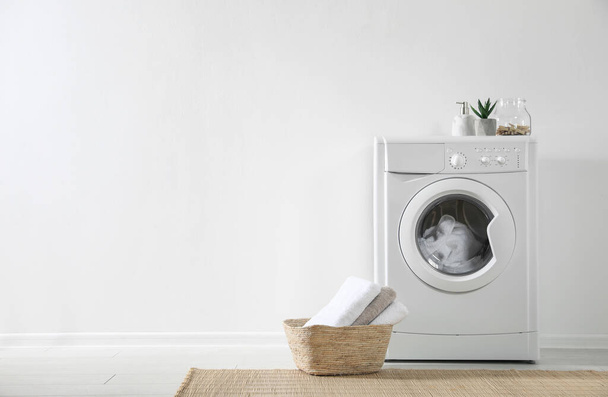 Modern washing machine and laundry basket near white wall indoors, space for text. Bathroom interior - Fotografie, Obrázek