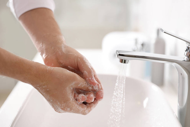 Man washing hands with soap over sink in bathroom, closeup - Fotó, kép