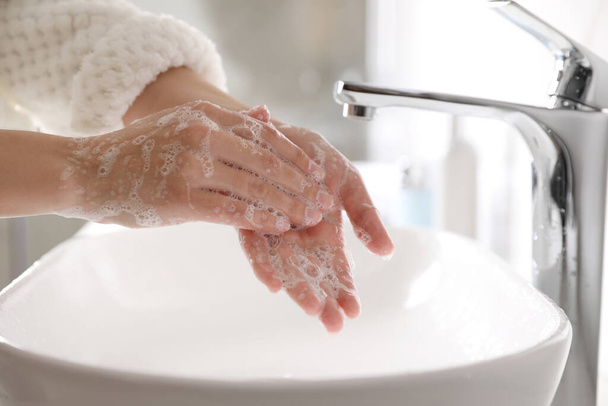 Woman washing hands with soap over sink in bathroom, closeup - Фото, изображение