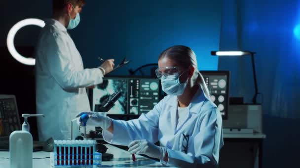 Scientist and student working in lab. Doctor teaching intern to make blood analyzing research. Laboratory tools: microscope, test tubes, equipment. Coronavirus, vaccine research, bacteriology - Záběry, video