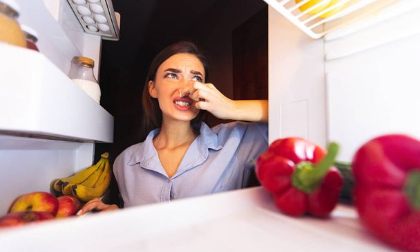 冷蔵庫の近くで鼻を閉じる女性,悪い匂いを感じる - 写真・画像
