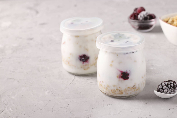 Granola crispy honey muesli with natural yogurt and frozen berries in in two closed glass jars on a gray background, healthy food, Space for text - Foto, Imagen