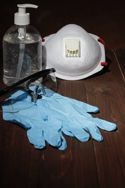 recommended personal protection kit formed by hygiene gel, medical mask, nitrile gloves and security glasses to prevent contagion by bacteria and virus. all over wooden ground and background - Photo, Image