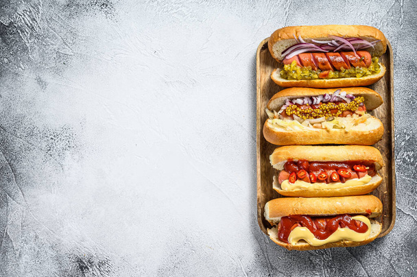 Hot Dogs mit verschiedenen Belägen. Leckere Würstchen mit Schweine- und Rindfleisch. Weißer Hintergrund. Ansicht von oben. Kopierraum. - Foto, Bild