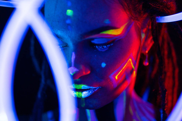 Portrait of a Girl with Glowing Tubes in Neon UF Light. Model Girl with Dreadlocks and Fluorescent Creative Psychedelic MakeUp, Art Design of Female Disco Dancer Model in UV, Colorful Abstract Make-Up - Zdjęcie, obraz