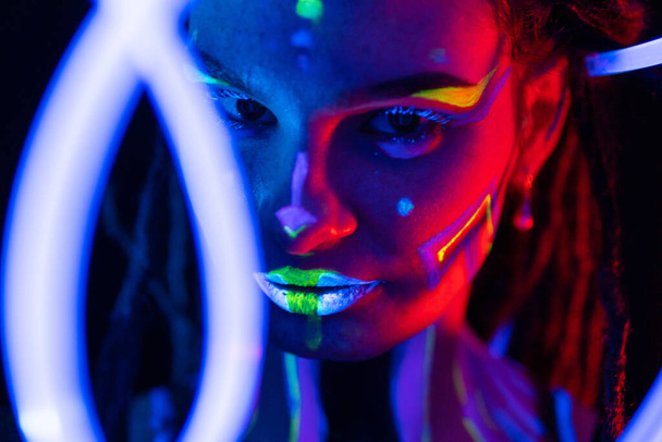 Portrait of a Girl with Glowing Tubes in Neon UF Light. Model Girl with Dreadlocks and Fluorescent Creative Psychedelic MakeUp, Art Design of Female Disco Dancer Model in UV, Colorful Abstract Make-Up - Foto, Bild