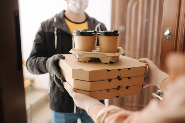 Delivery man in mask and gloves give pizza and coffe to customer. Stay home - Фото, изображение