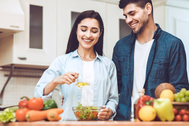 Happy young couple preparing salad together at home - Foto, Imagen