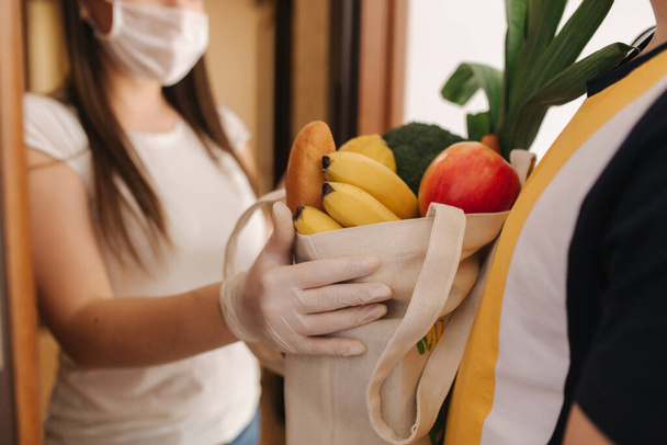Delivery man in mask and gloves give fresh food to recipient and young woman customer. Stay home, Online shopping concept - Photo, image