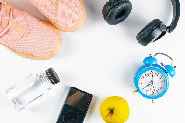 The diet plan. Pinc sneakers, headphones, bottles with water, clock and apples with measuring tape on a white background. Slimming and detox concept. - Photo, Image