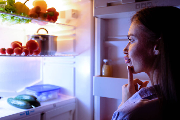Pensive κορίτσι ψάχνει στο ψυγείο για αργά σνακ - Φωτογραφία, εικόνα