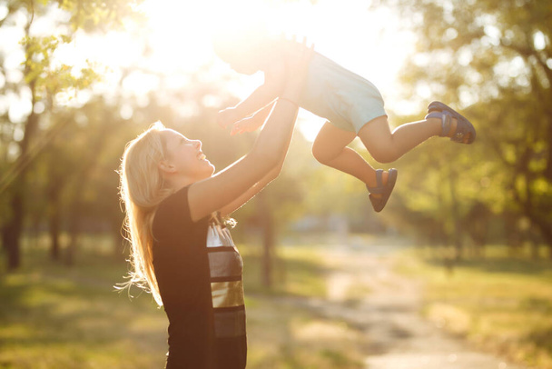 Happy mother throws baby up, laughing and playing in the summer on the nature. Happy mother's day. Family holiday and togetherness. - Foto, imagen