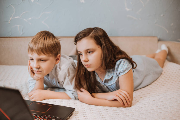Het meisje en de jongen die thuis webinar kijken op laptop tijdens CoVid-19 quarantaine, afstandsonderwijs online met een laptop, een kind dat huiswerk maakt voor school. Kinderen bleven thuis. Thuisonderwijs - Foto, afbeelding