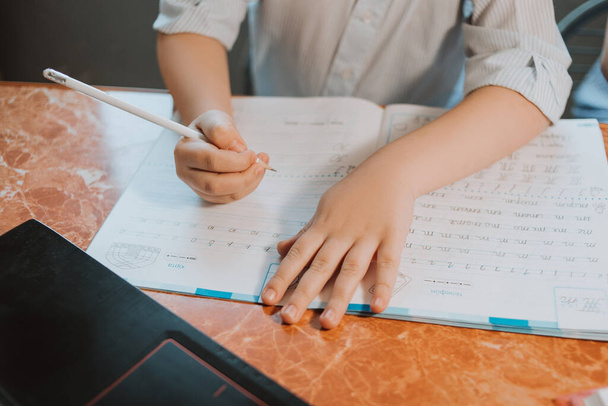少年はCoVid-19隔離中に自宅のノートパソコンでオンラインで遠隔学習学校で宿題をしている子供に宿題を書いています。子供たちは家にいた。少年はキリル文字で書く. - 写真・画像