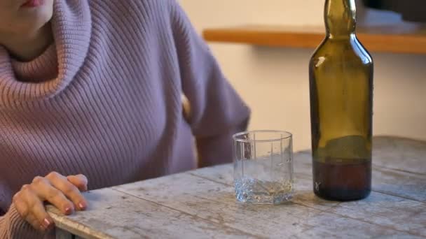 Droevige vrouw in jeans en roze trui komt thuis, legt dollars en sleutels op tafel en giet whisky op haar glas uit de groene fles vanwege de problemen, vrouwelijke alcoholverslaving - Video