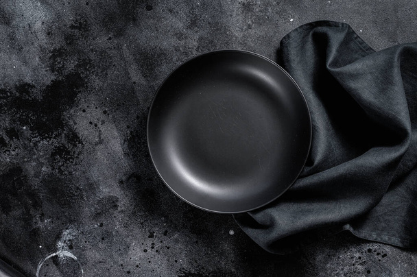 Black plate and a towel on textured black background. Top view. Copy space. - Photo, Image