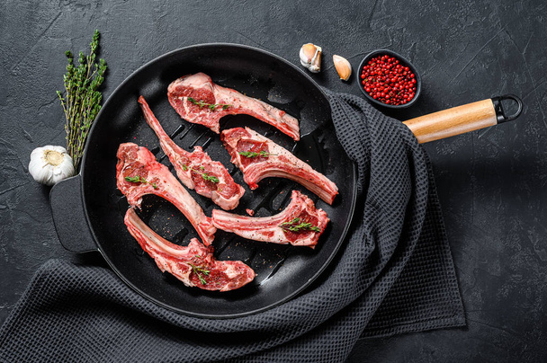 Raw fresh lamb rib chops with salt, pepper and herbs in a pan. Black background. Top view. - Foto, Bild