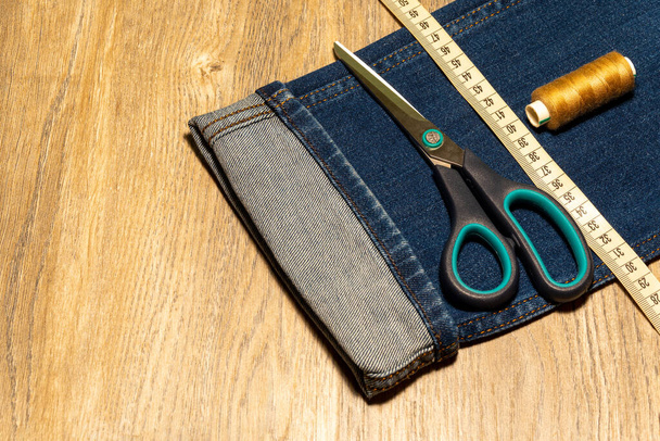 Close up to jeans, scissors, measuring tape and thread on wooden background  - Photo, Image