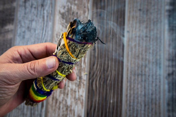 Hand hält Bündel brennenden Salbeis vor Holzhintergrund - Foto, Bild