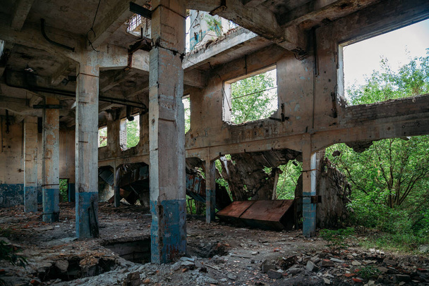 Oude verlaten ruïne industrieel gebouw begroeid met planten en bomen. - Foto, afbeelding