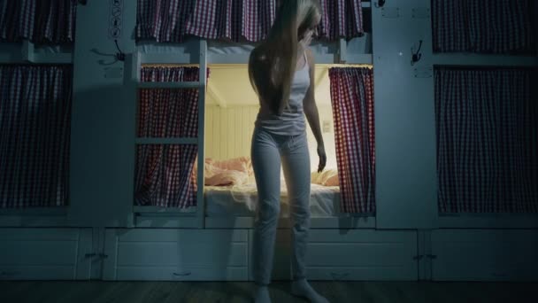 Młoda dziewczyna kładzie się w łóżku i zasypia w przytulnym pokoju hostelu - Materiał filmowy, wideo