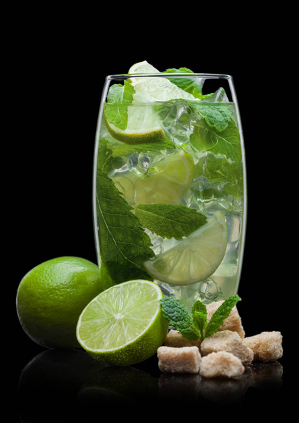 Highball glass of Mojito summer alcoholic cocktail with ice cubes mint and lime on black with cane sugar and raw limes. - Фото, зображення