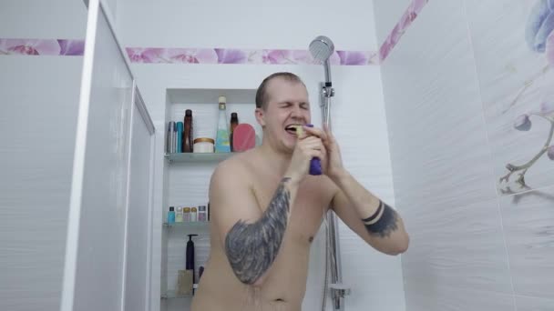 Νεαρός όμορφος χοντρός άντρας κάνει ντους στο μπάνιο. Συναισθηματικά τραγουδά και χορεύει - Πλάνα, βίντεο