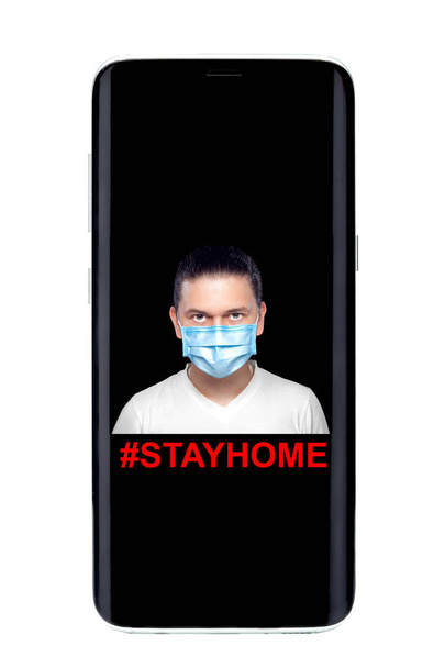 Черный смартфон на экране предупреждающее сообщение остаться дома с портретом человека в медицинской маске, мобильный телефон изолирован на белом фоне
. - Фото, изображение