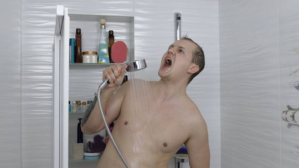 Fiatal, jóképű, kövér férfi zuhanyozik a fürdőszobában. Érzelmileg énekel és táncol - Fotó, kép