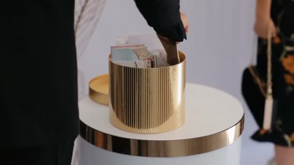 O hóspede coloca o envelope com dinheiro dentro da cesta com presentes de dinheiro para gromm e noiva. Bela caixa de forma de cone dourado cheio de envelopes com dinheiro
 - Filmagem, Vídeo