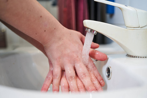 Lavado cruzado de manos para la prevención del coronavirus en un fregadero blanco con toallas rojas y negras en la parte posterior
 - Foto, Imagen